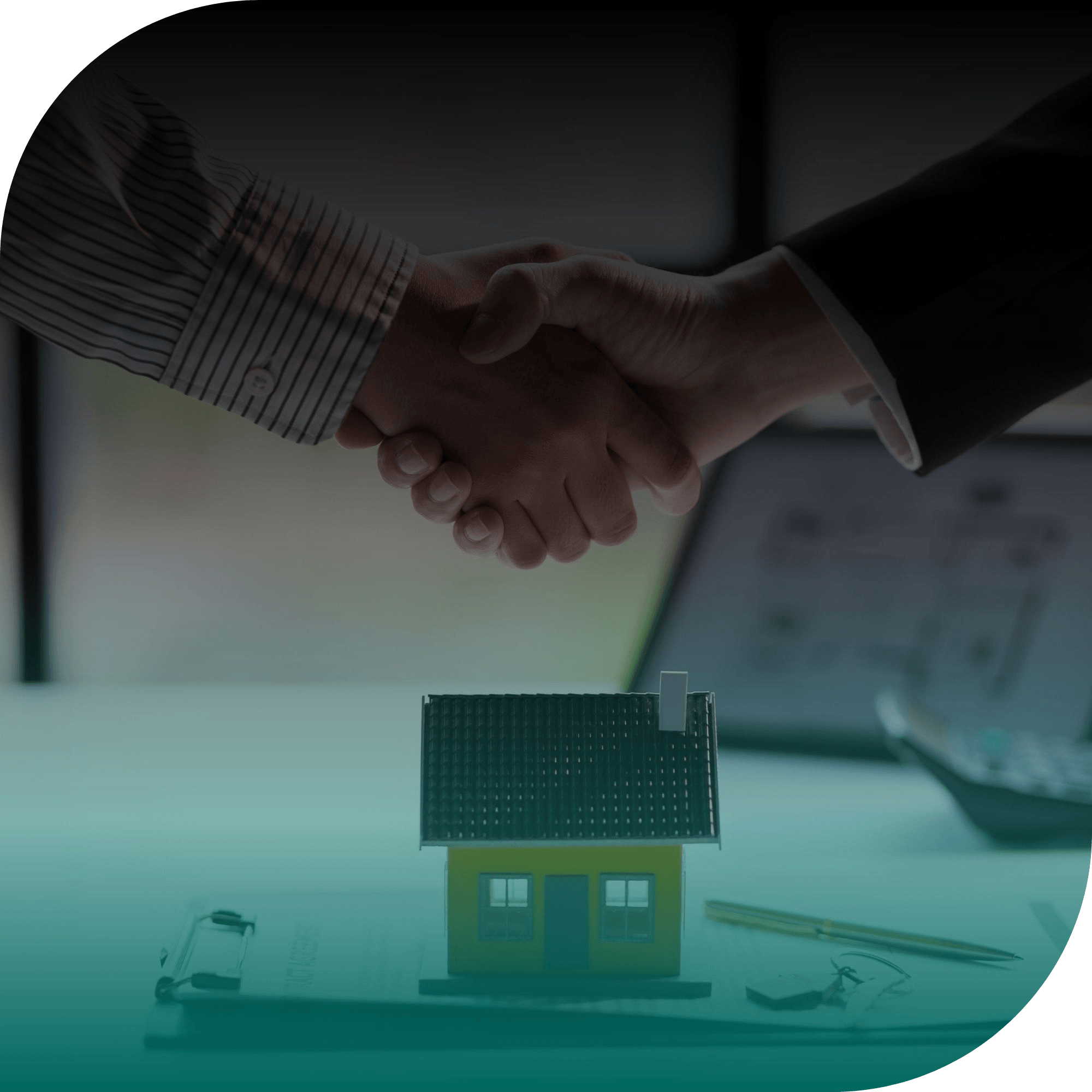 Two people shake hands above a desk with a small model house, scattered paperwork, and office tools, suggesting a real-estate or business agreement.