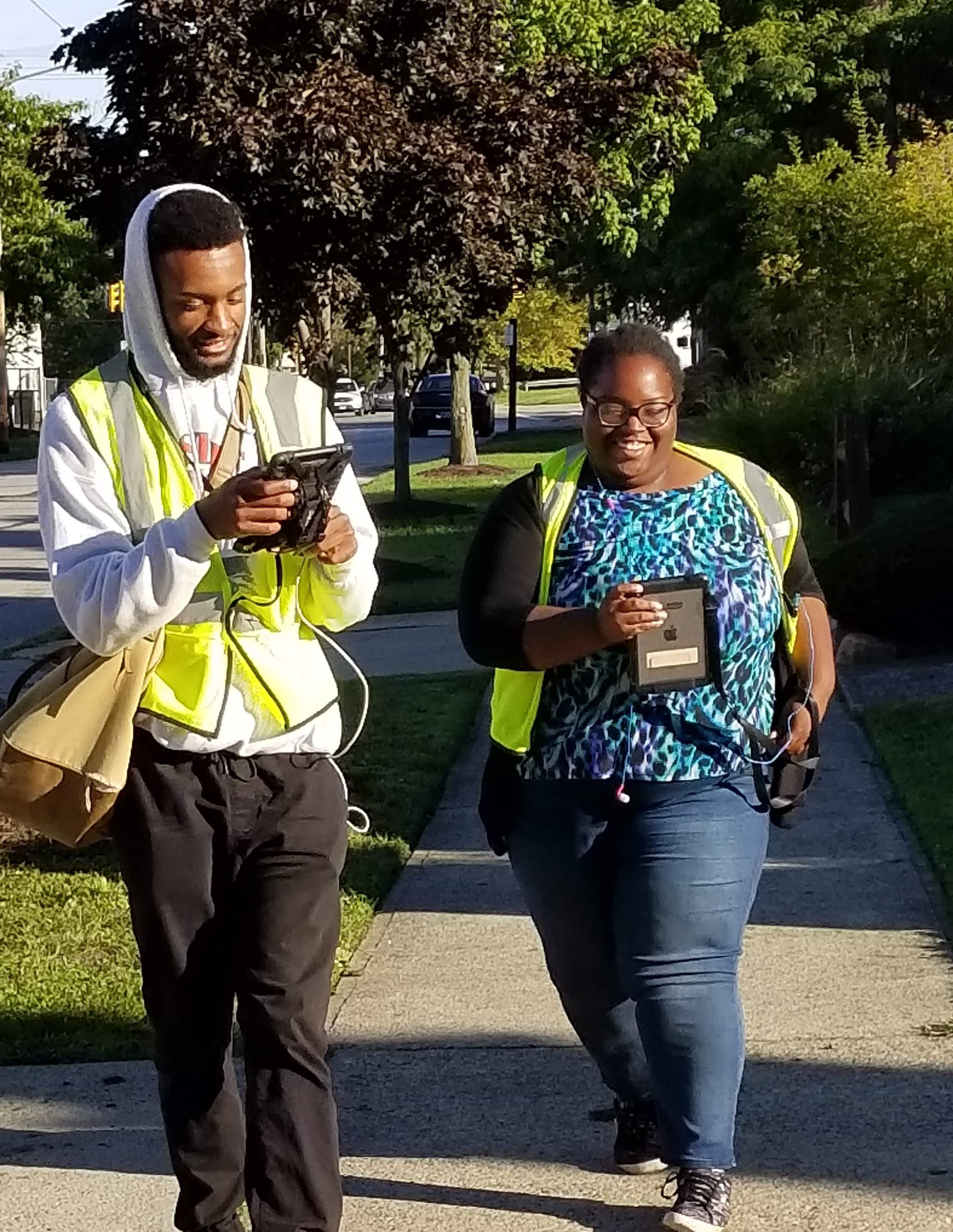 Two surveyors walk down the sidewalk while laughing and looking at the Regrid Mobile App